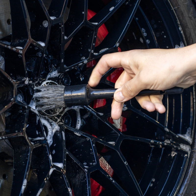 Using a detailing brush on a soapy black alloy wheel