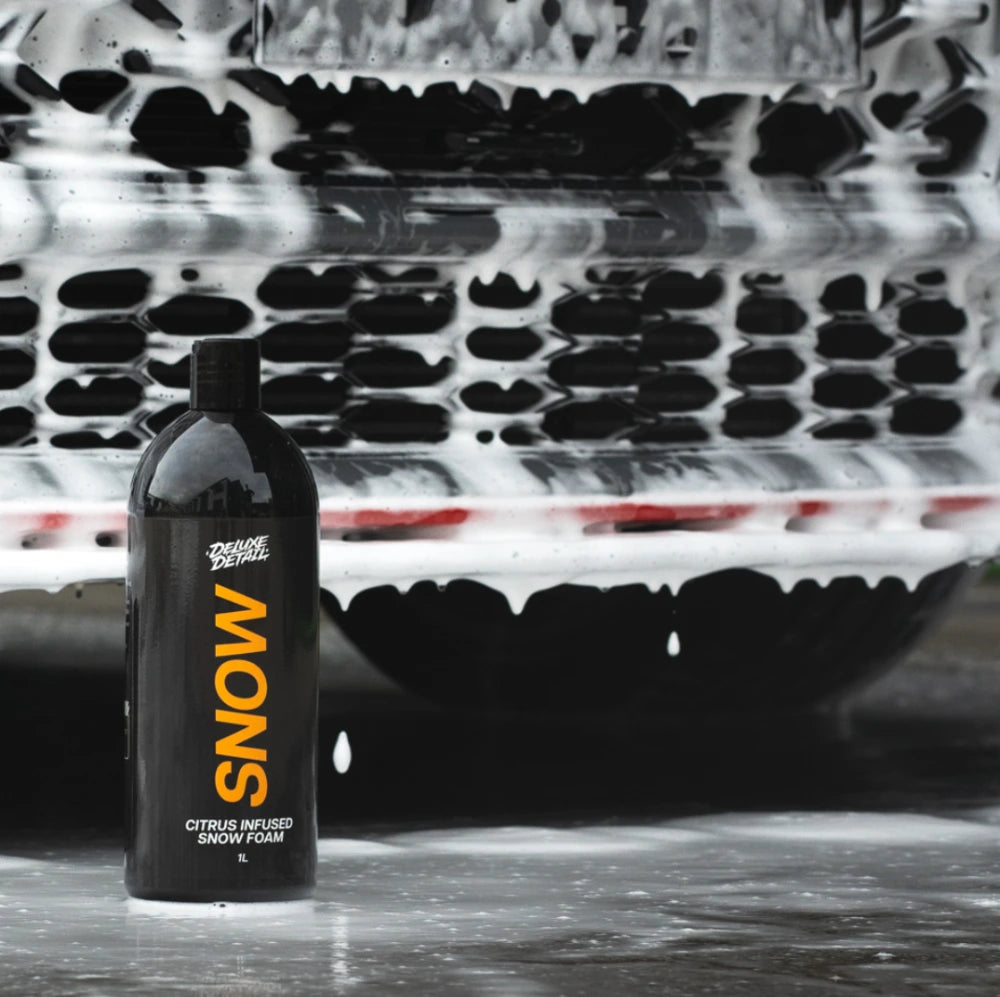 Deluxe Detail SNOW snow foam bottle in front of a car covered in thick white foam