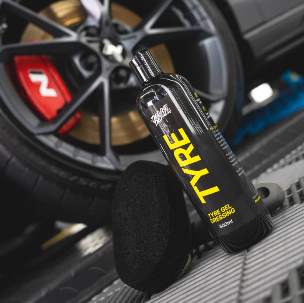 Deluxe Detail TYRE gel dressing and foam applicator pad resting against a tyre and alloy wheel