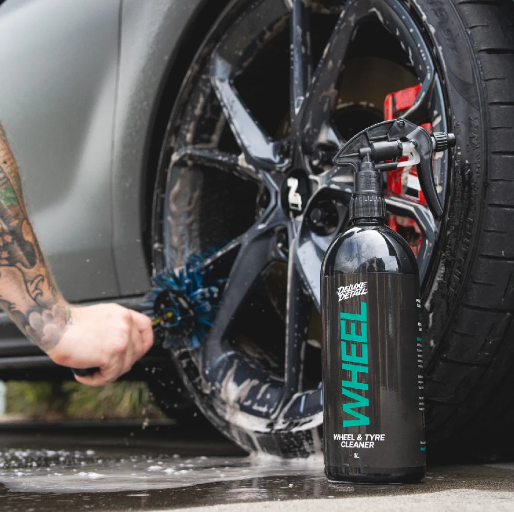 Deluxe Detail WHEEL cleaner beside an alloy wheel being scrubbed with a wheel brush