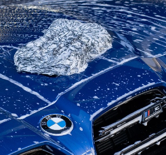 Deluxe Detail microfibre wash pad resting on the foam covered bonnet of a blue BMW M car