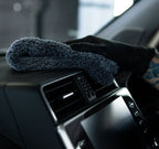 Gloved hand wiping a car dashboard vent with a plush microfibre interior cloth