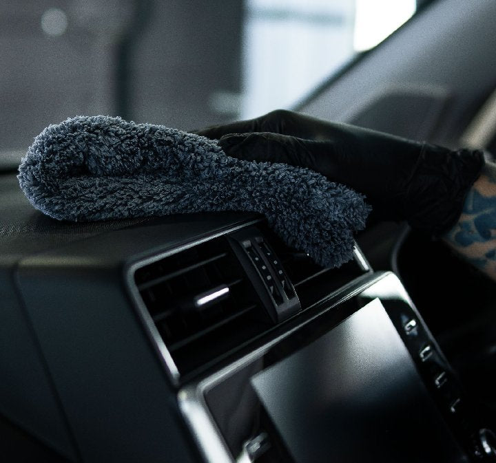 Gloved hand wiping a car dashboard vent with a plush microfibre interior cloth