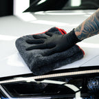 Gloved hand buffing white car paintwork with a red edged plush microfibre cloth