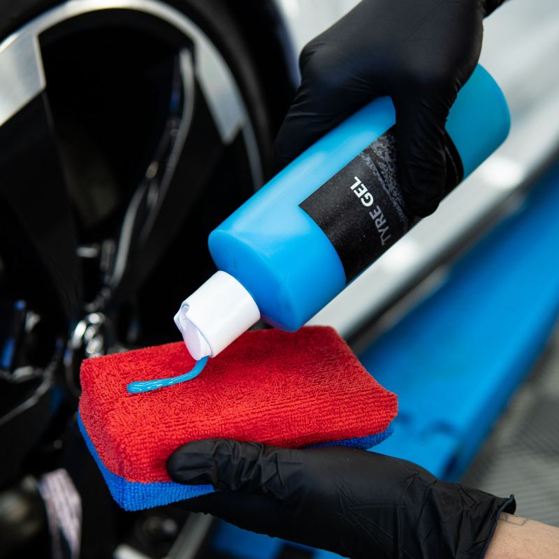 Squeezing tyre gel onto a large red microfibre applicator pad beside a wheel